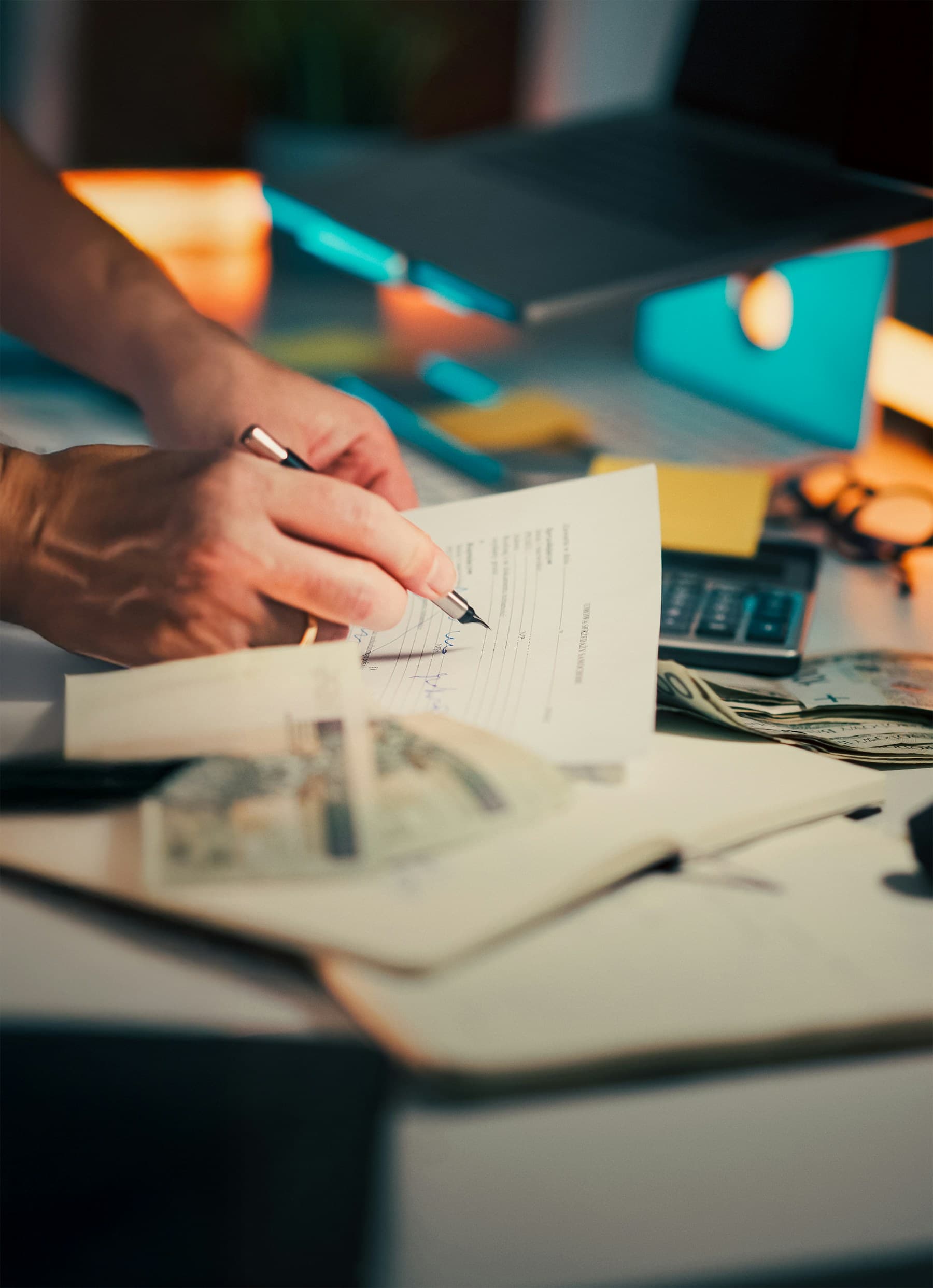A person signing documents on a desk with a calculator and papers.